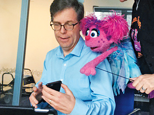 Michael Levine looking at a cell phone with muppet Abby Cadabby