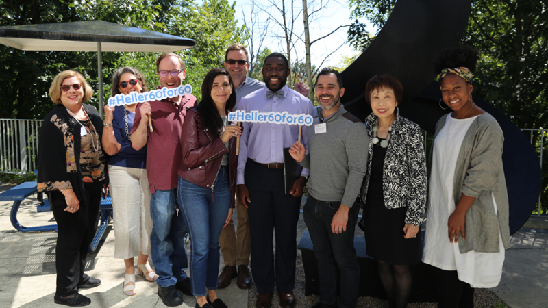 Members of the Heller Alumni Association Board holding Heller 60th Anniversary signs