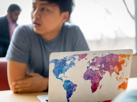 a laptop with a colorful world map in front of a student