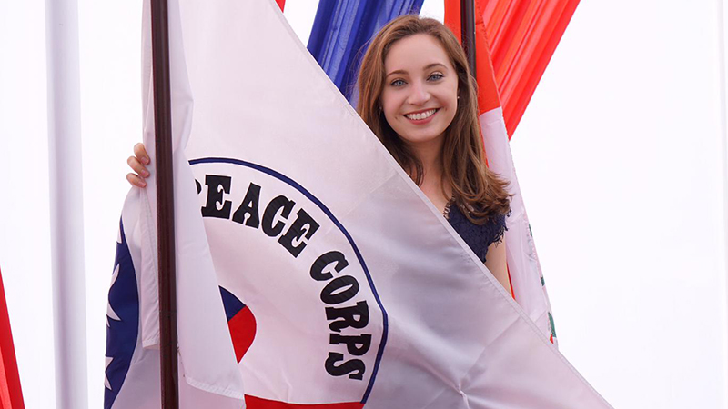 Nicole Levesque posing with a Peace Corps flag