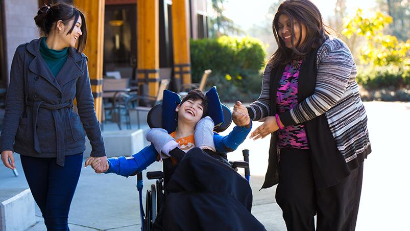 Child in wheelchair laughing with two adult women