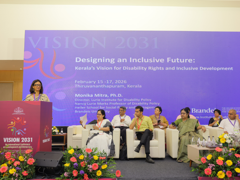 Monika Mitra on a Stage Fielding Questions from an Audience; Beside Her is an Indian Sign Language Interpreter