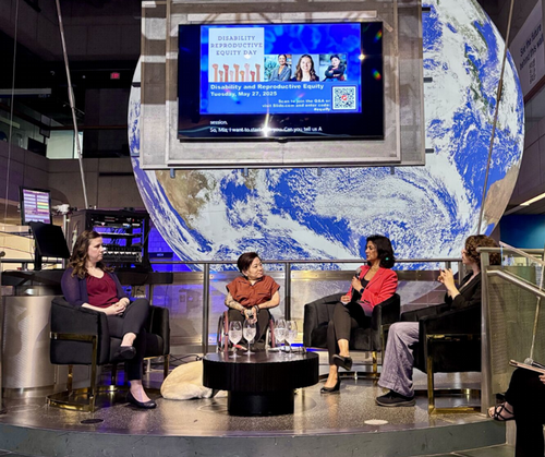 Panelists and interviewer seated on a platform. A large globe and TV screens are visible behind the speakers. 