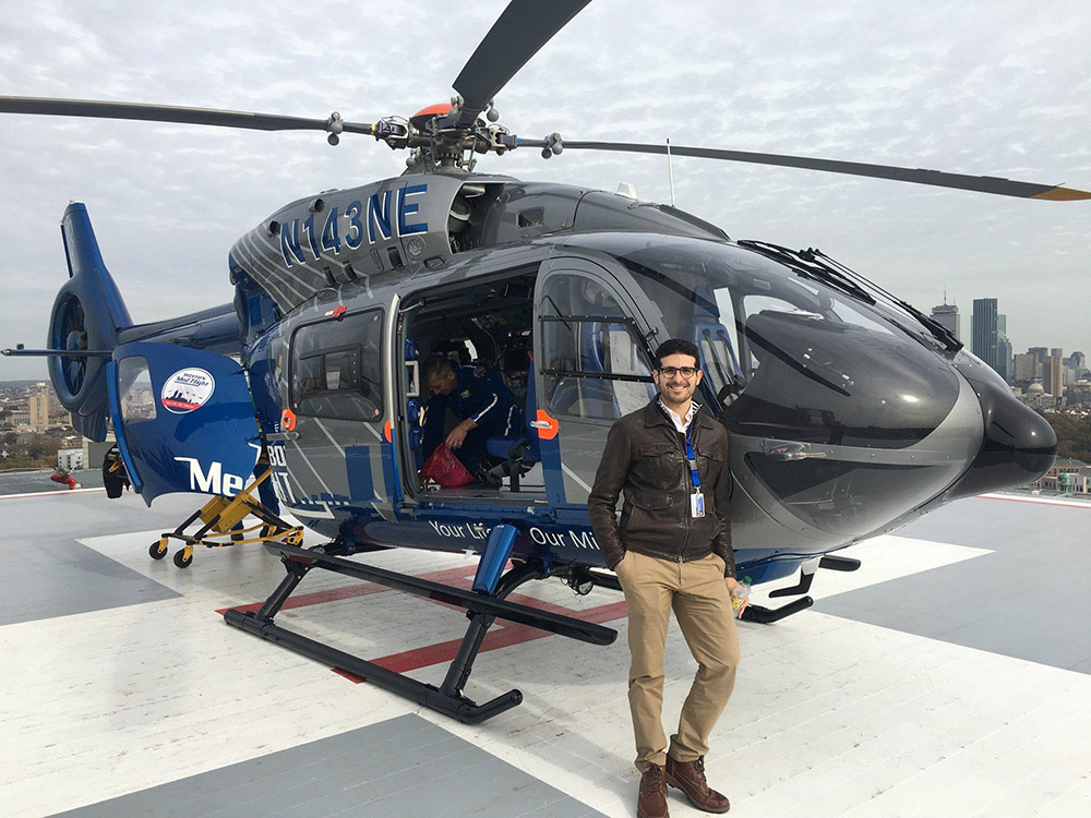 Matthew Kriegsman in a leather jacket and khakis in front of a gray helicopter