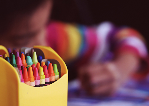 Photo of a box of crayons with a child coloring in the background