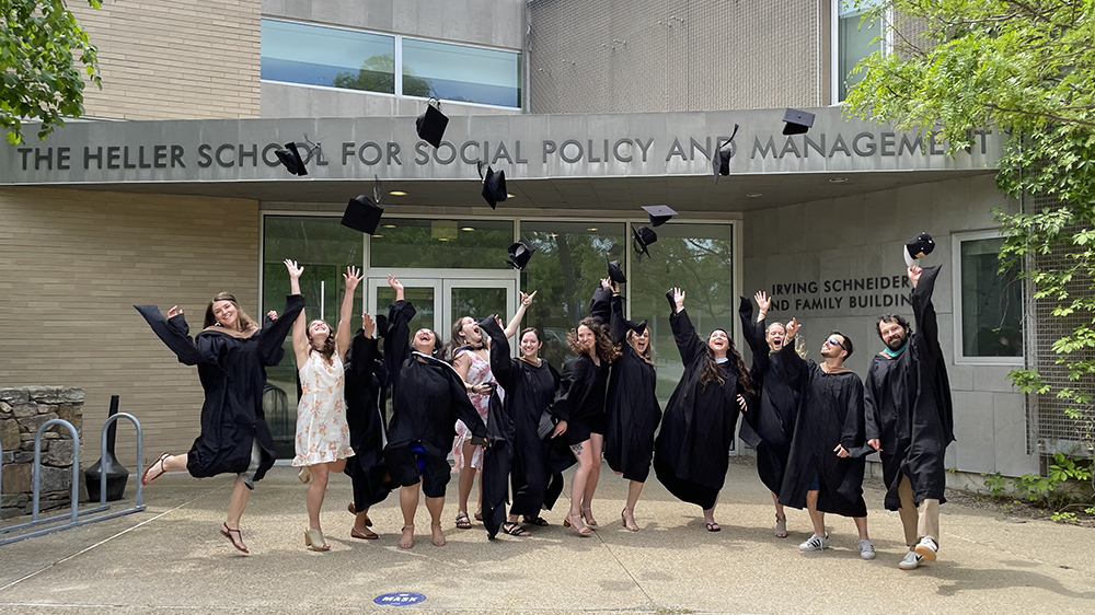 Students in graduation regalia throwing caps in the air in front of the Heller School for Social Policy and Management
