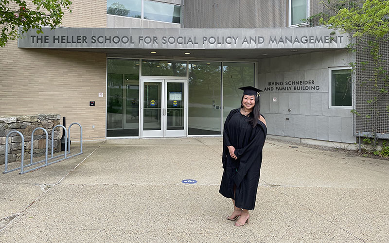 Peggy Zhang, MBA/MA SID'21, in graduation regalia in front of the Heller School for Social Policy and Management entrance