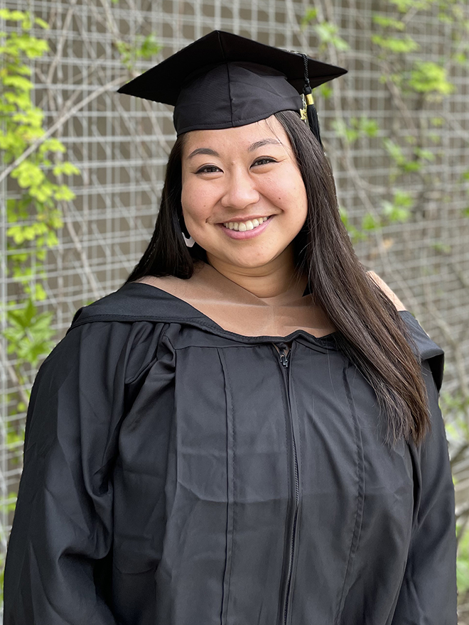 Peggy Zhang, MBA/MA SID'21, in a black commencement cap and gown in front of vines outdoors