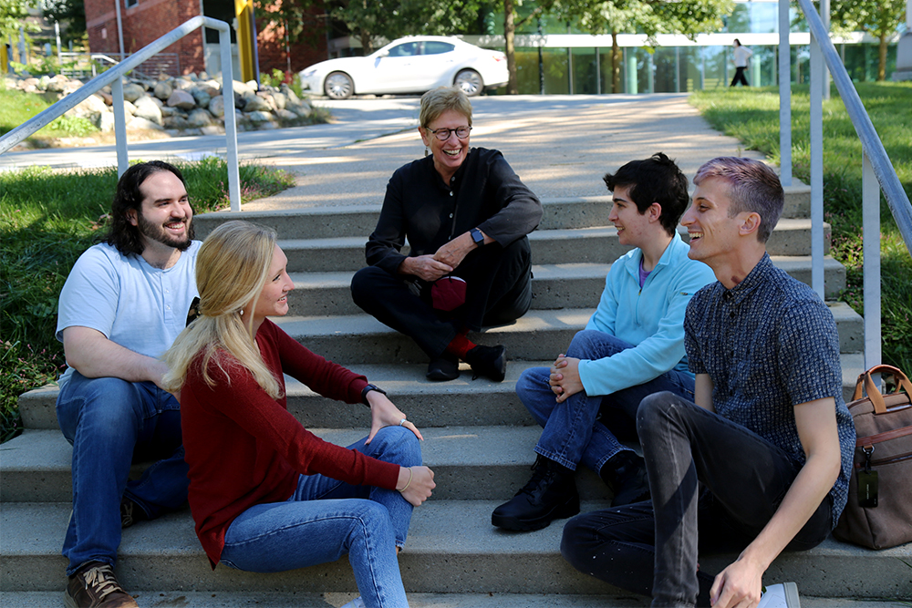 Four students and a professor sitting outside and chatting