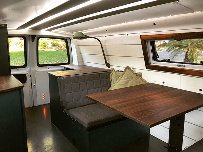 A table, padded seat, pillows, desk lamp inside a van