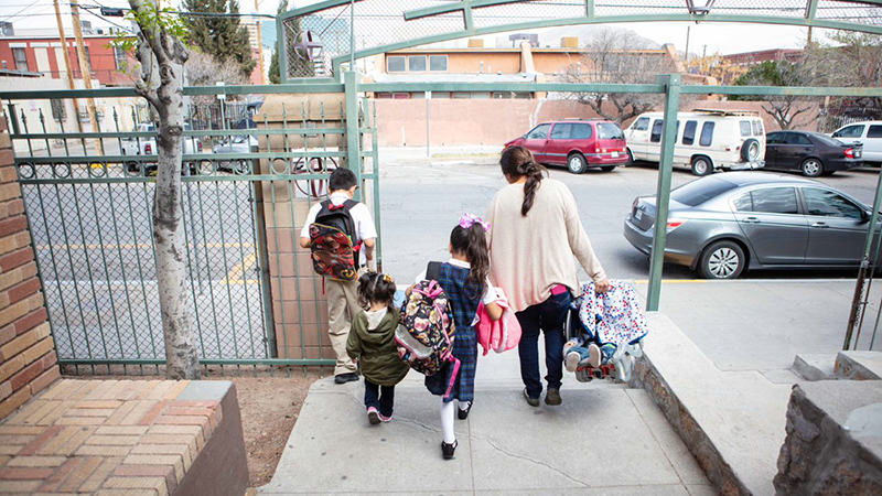 A mother holds a carseat while walking with three other children out of a gate