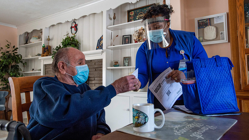 a nurse hands a patient his covid vaccine card while treating him in his home