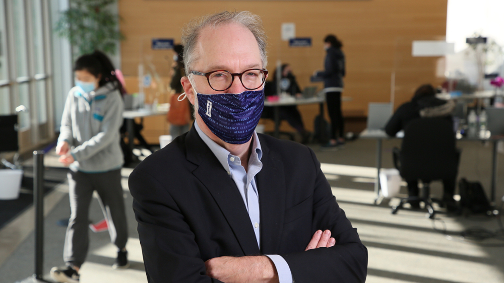 David Weil in a Brandeis face mask in Zinner Forum with COVID-19 testing behind him