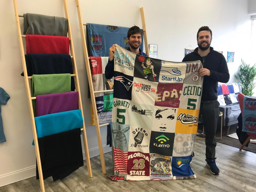 Two men holding a blanket made of sports shirts