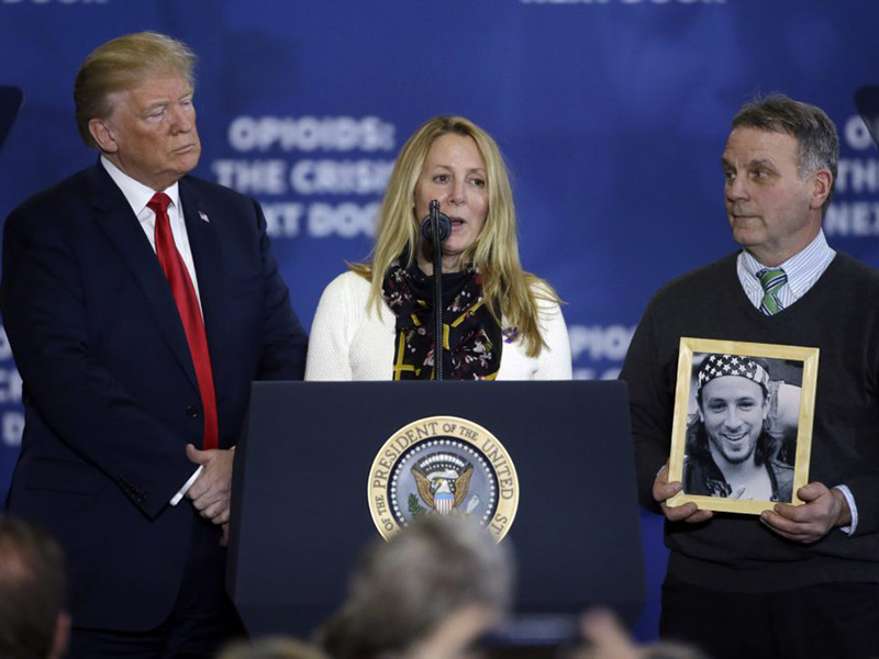 A woman giving a speech with Donald Trump and another man who holds a portrait next to her
