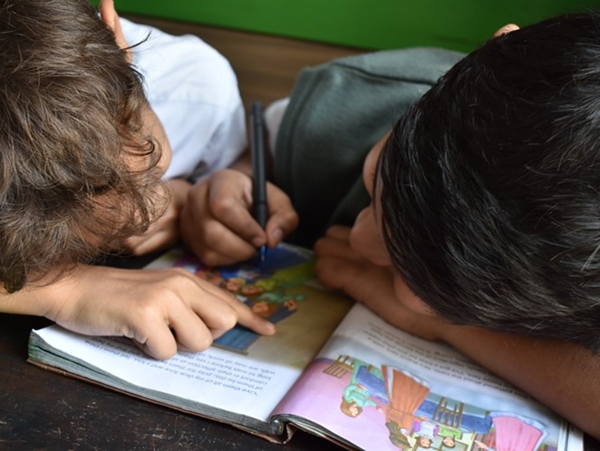 two kids leaning and writing on a book