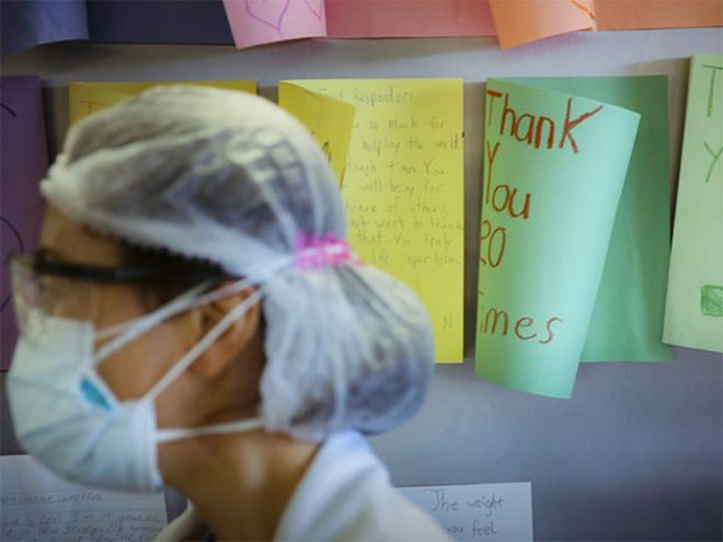 A nurse with a facemask in front of thank you cards