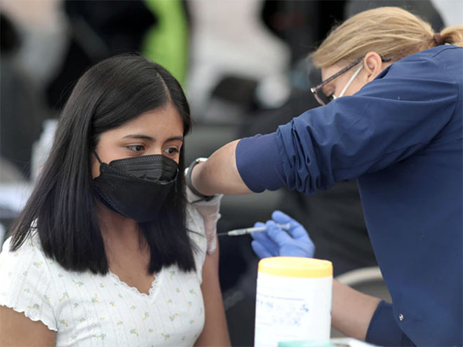 A woman wearing a face mask receives a vaccination in her arm