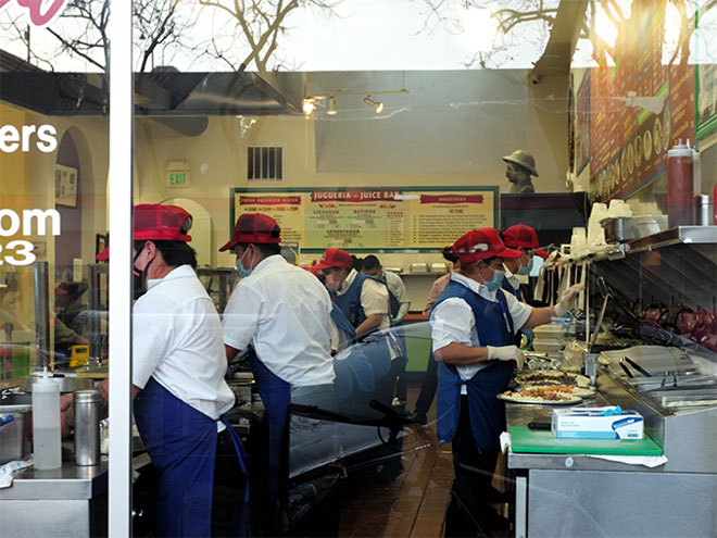 Workers in red hats and blue aprons working in a pizza shop