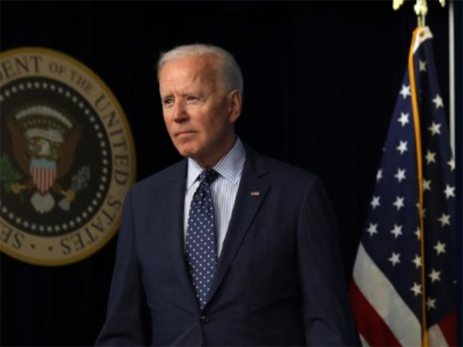 President Joe Biden in a suit in front of an American flag and presidential seal