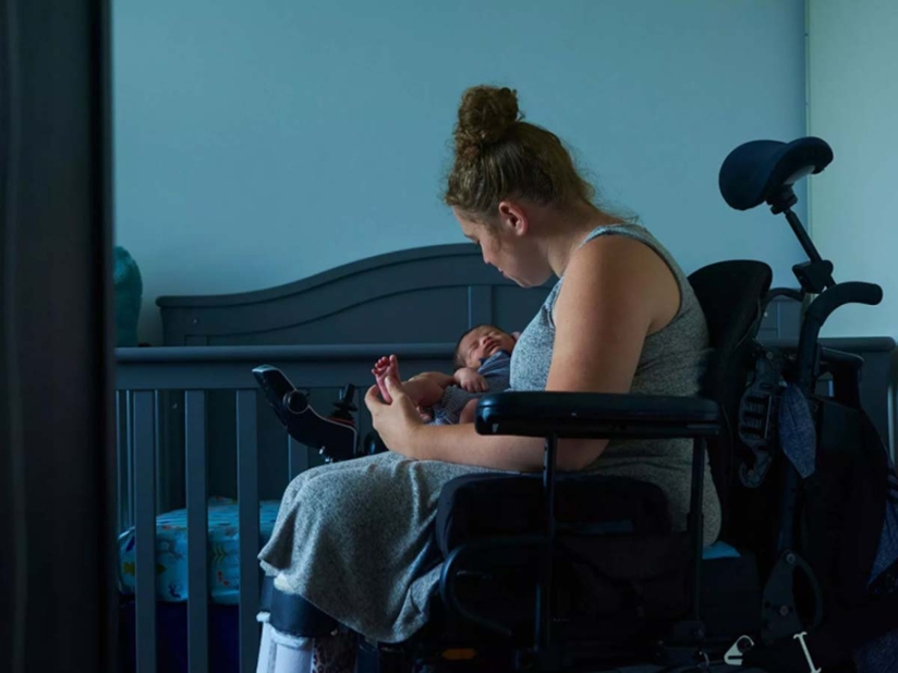 A woman in a power chair holds an infant