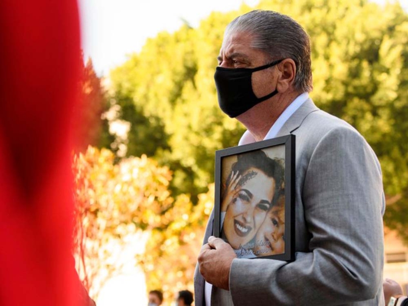 A man holds a photo of a woman at a news conference
