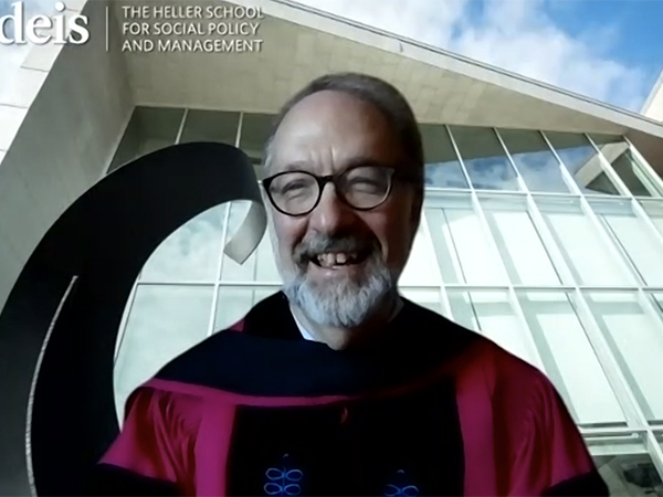 Dean David Weil in a red commencement robe in front of a virtual Zoom background of the soaring windows of the Zinner Forum
