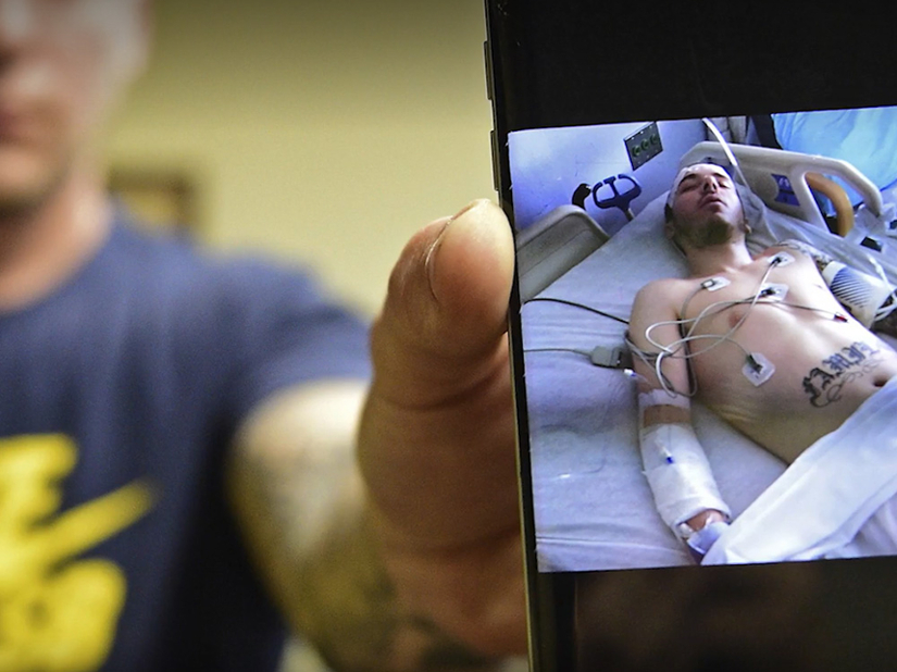 A man holds up a picture on his phone showing him on a hospital bed