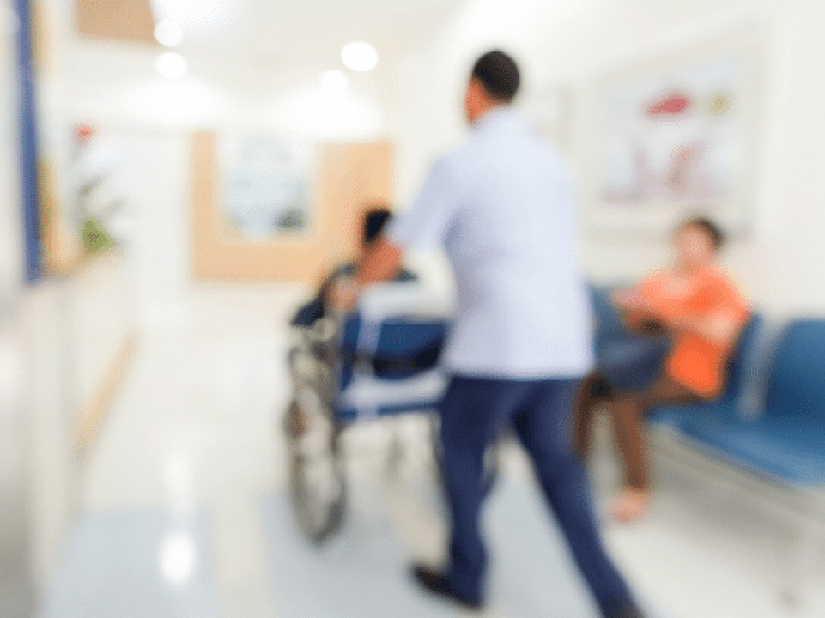 Blurred image of someone in a wheelchair being pushed down the hall in a doctor's office