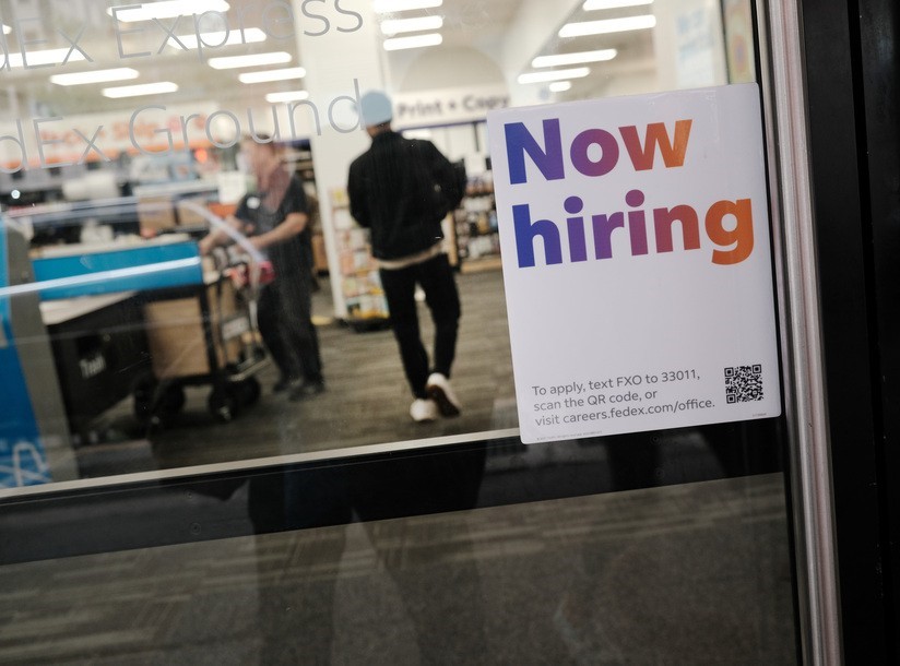 A store's door with a sign that reads "NOW HIRING"