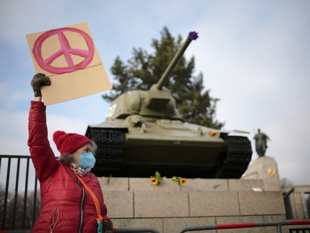 A woman holds a peace sign in front of a tank