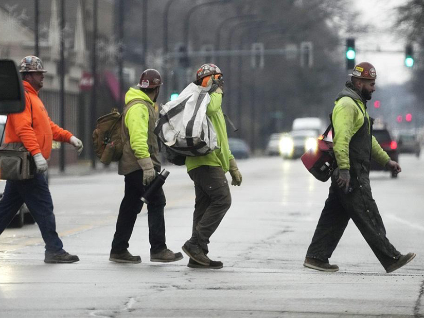 Workers walk across a street wearing hi-visibility gear