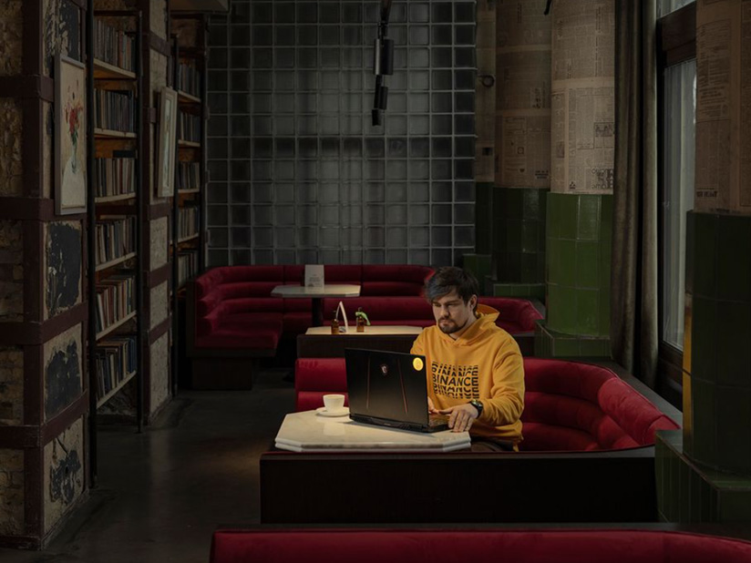 A man wearing a "Binance" hoodie types on a laptop
