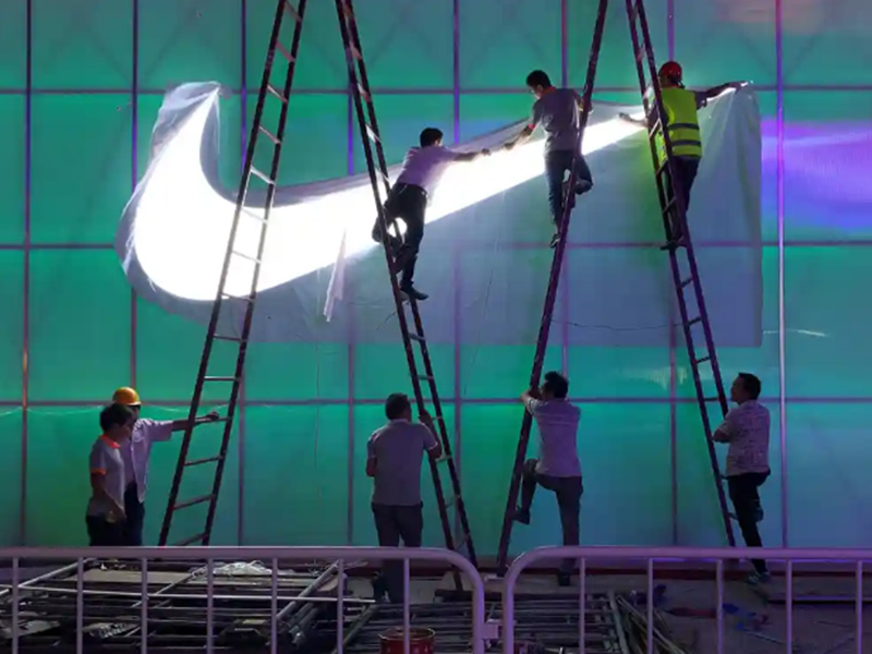 Workers install a light in the shape of the Nike swoosh logo to a wall