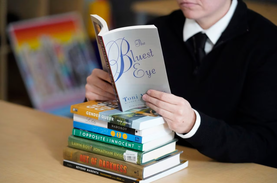 A person holds open a copy of The Bluest Eye on top of a stack of other books