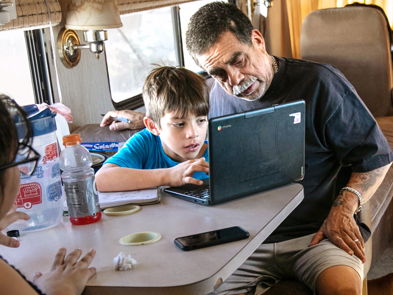 A father helps his son with homework on a laptop in their home