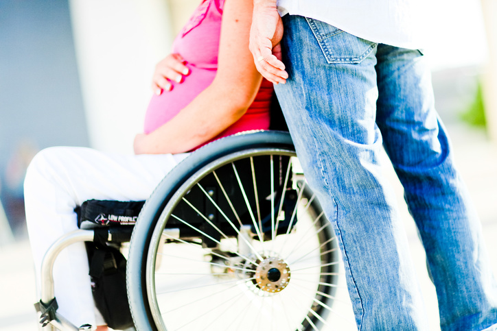 A pregnant women using a wheelchair and her partner standing with her.