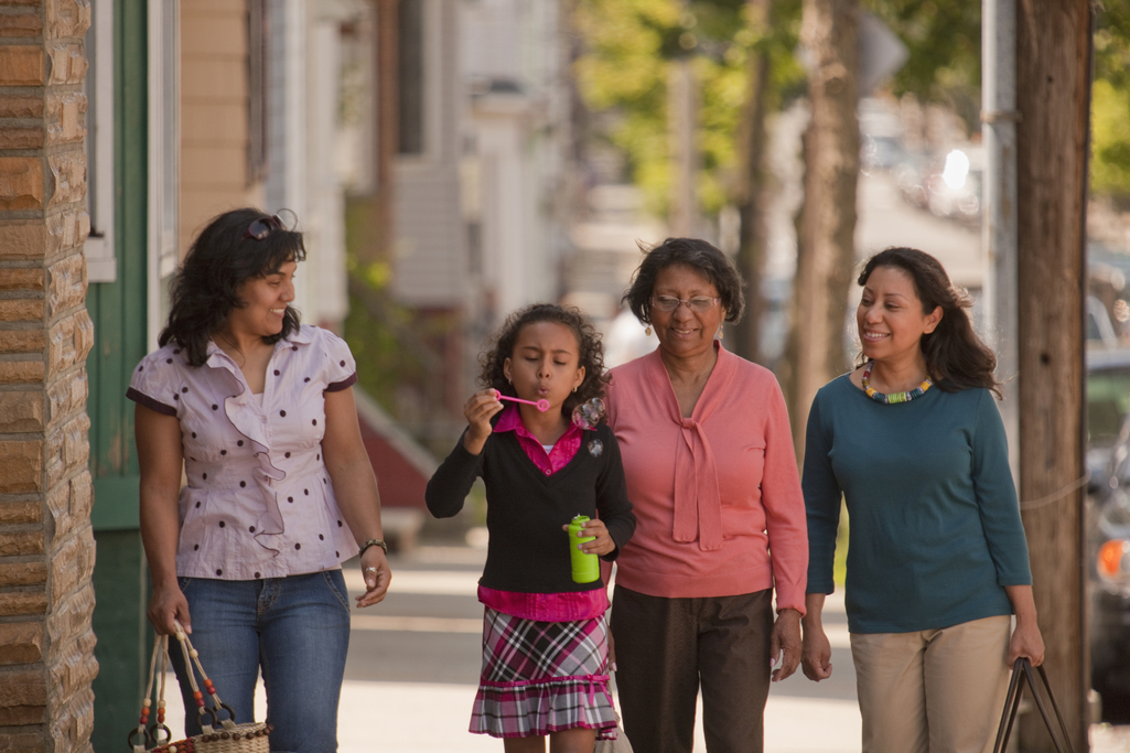 A young girl blows bubbles walking down the sidewalk with her family