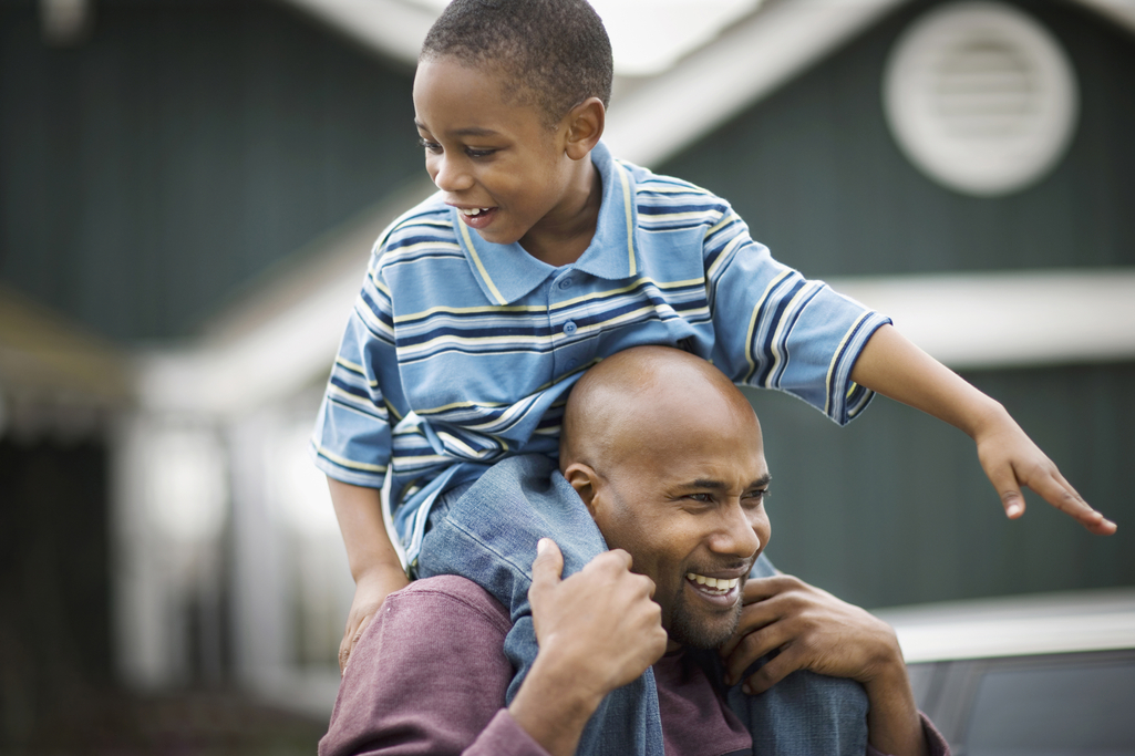 A boy sits on his father's shoulders.