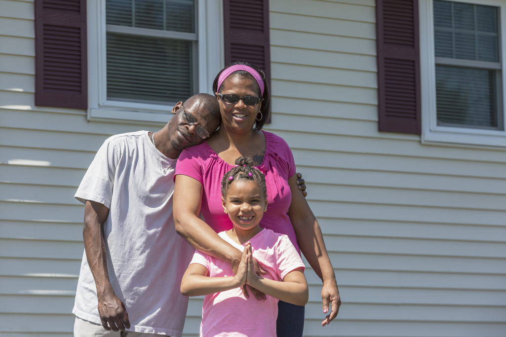 A young girls stands in front of her house with her parents.