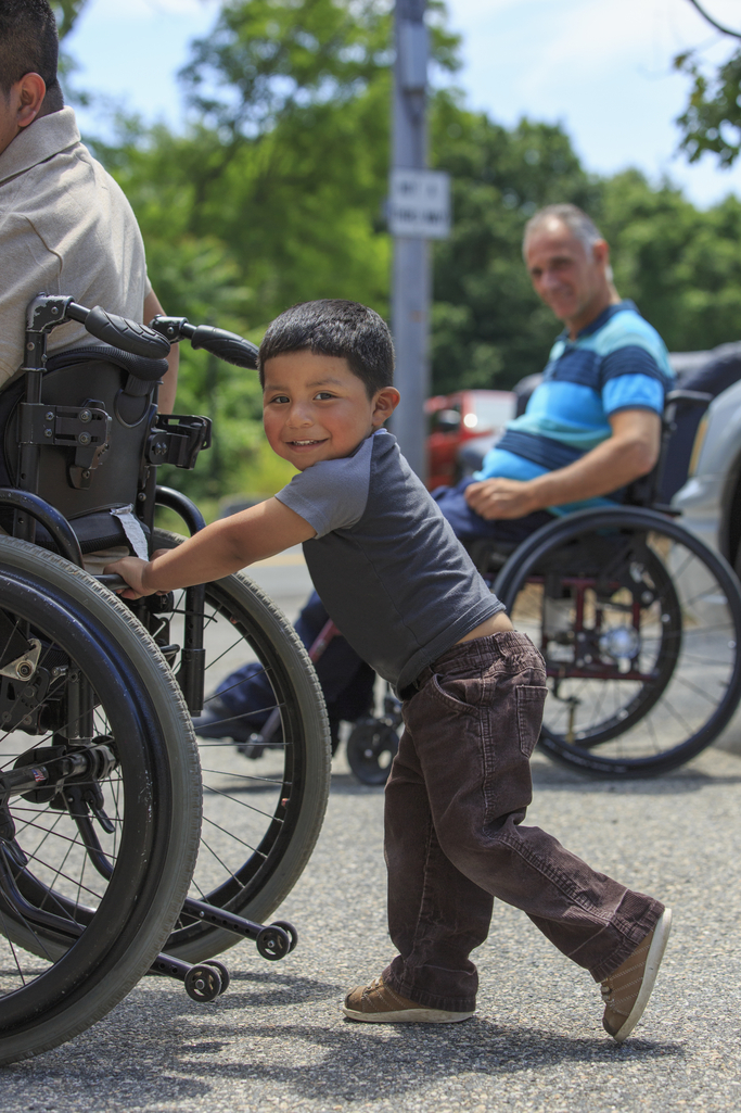 A young boy plays behind his father who is using a wheelchair