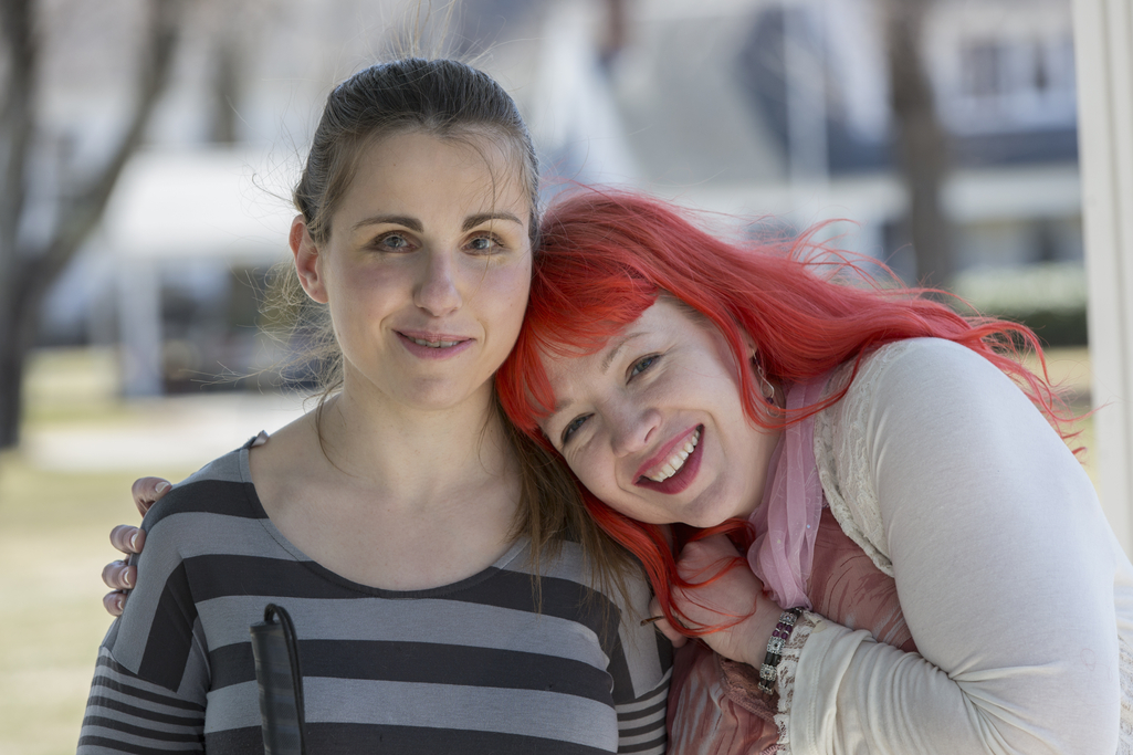 Two women with visual impairments lean in toward each other and smile at the camera