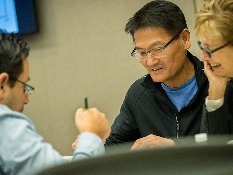 three EMBA students talking to each other in the classroom
