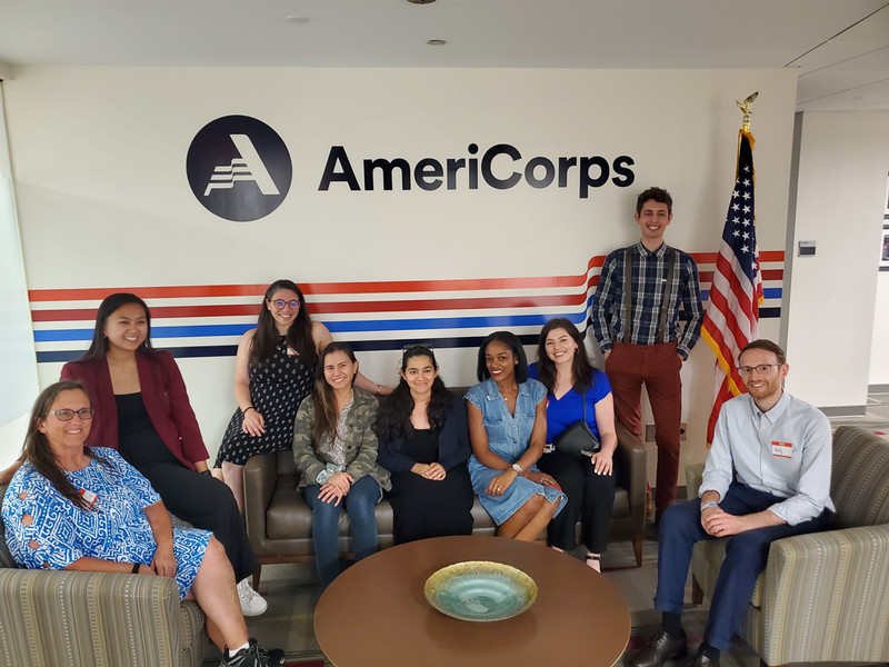 9 americorps alum segal fellows sitting in front of the americorps logo. 