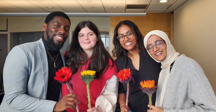 Four 2025 Brandeis Segal Fellows smiling in a line and holding red and orange sunflowers