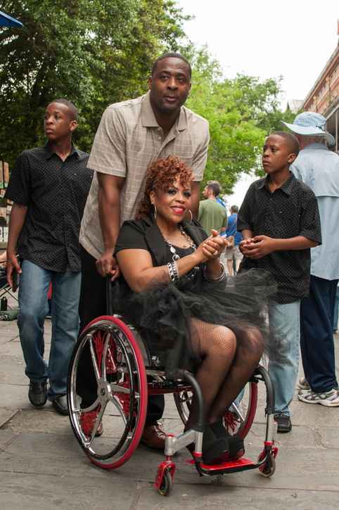 A woman using a wheelchair posing outdoors with her husband and two sons