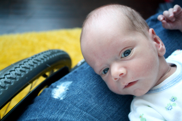A newborn infant lays on his mother's lap while she is using a wheelchair