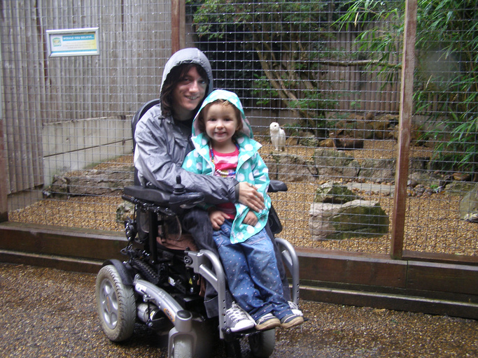 A mother using a wheelchair holds her daughter on her lap at the zoo