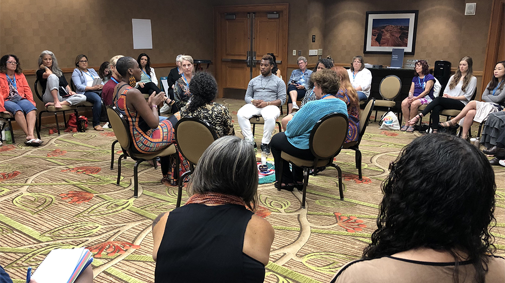 A group of people talking while sitting in a circle chairs, within a larger circle of chairs.