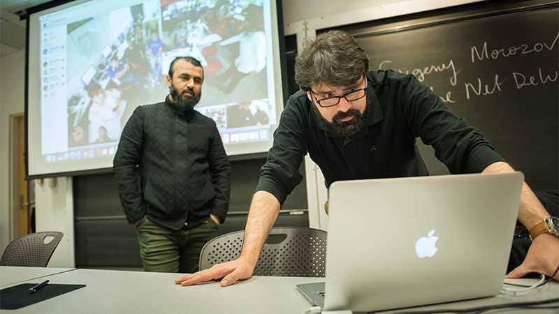 professor leaning over laptop in front of class